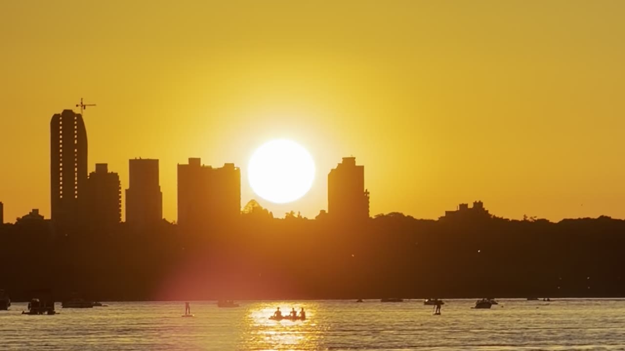 Atardecer sobre el skyline de Paraná visto desde el río, con el sol reflejado en el agua